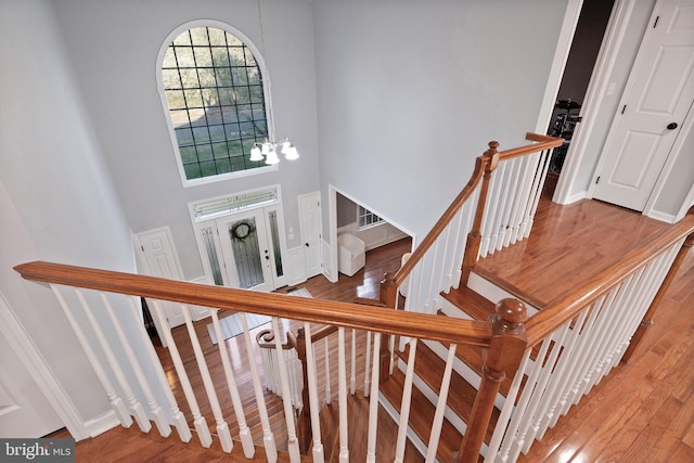 staircase with hardwood / wood-style floors, a notable chandelier, and a towering ceiling