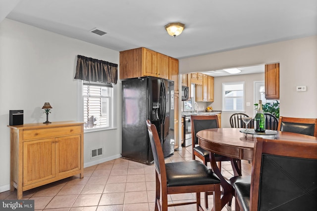 kitchen featuring light tile patterned floors, sink, black fridge, and stainless steel range oven