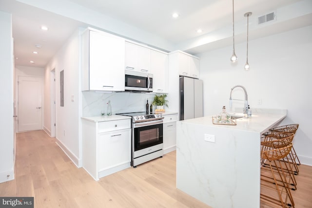 kitchen with light wood-type flooring, stainless steel appliances, sink, decorative light fixtures, and white cabinetry