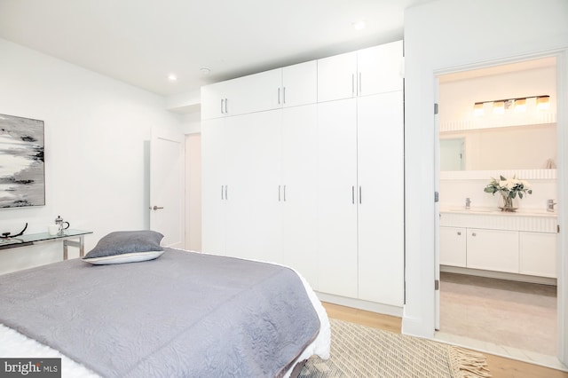 bedroom with ensuite bath, light hardwood / wood-style flooring, and sink