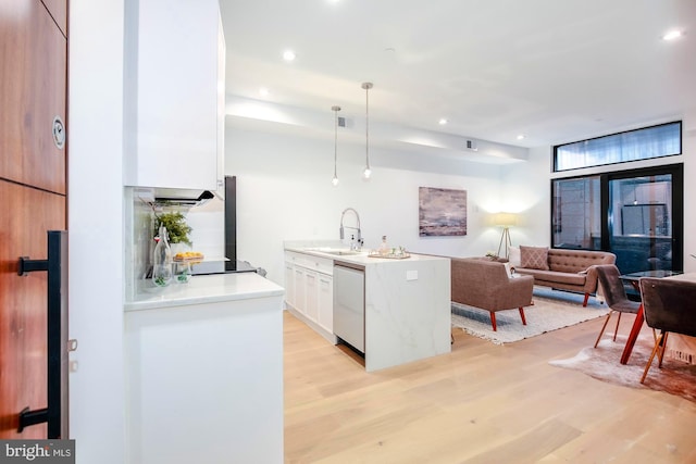 kitchen featuring white dishwasher, sink, light wood-type flooring, decorative light fixtures, and white cabinetry