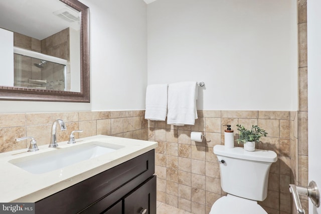 bathroom with vanity, toilet, a shower with shower door, and tile walls