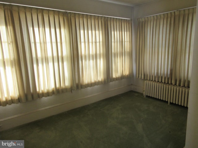 empty room featuring radiator, dark carpet, and a healthy amount of sunlight