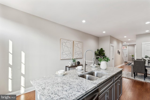 kitchen with sink, light stone counters, dark hardwood / wood-style flooring, stainless steel dishwasher, and a kitchen island with sink