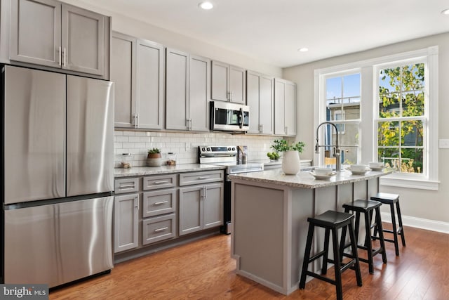 kitchen featuring hardwood / wood-style floors, gray cabinetry, a center island with sink, and stainless steel appliances