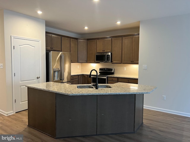 kitchen featuring light stone countertops, sink, stainless steel appliances, hardwood / wood-style floors, and an island with sink