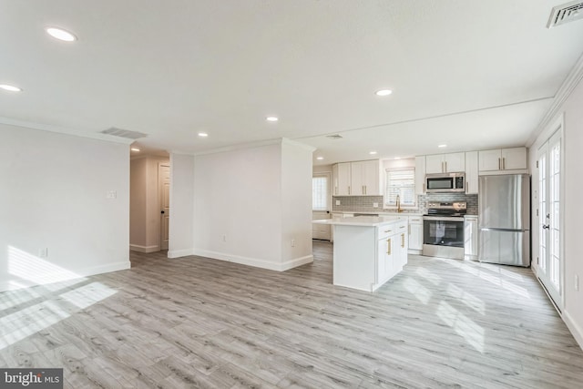 kitchen with white cabinets, a kitchen island, ornamental molding, appliances with stainless steel finishes, and light hardwood / wood-style floors