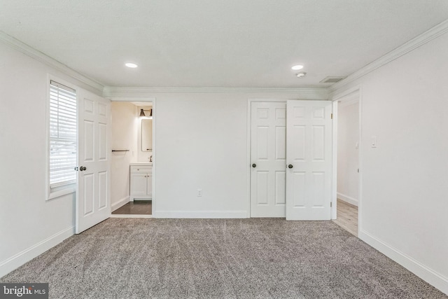 unfurnished bedroom featuring carpet flooring, ornamental molding, a textured ceiling, and ensuite bath