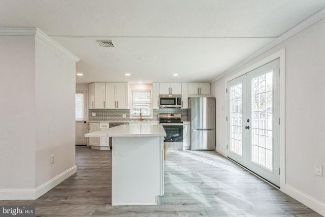 kitchen featuring french doors, white cabinets, light wood-type flooring, appliances with stainless steel finishes, and tasteful backsplash