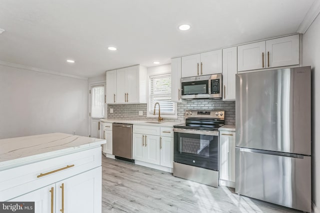 kitchen with white cabinets, sink, light wood-type flooring, ornamental molding, and stainless steel appliances