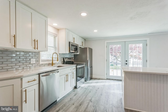 kitchen with sink, appliances with stainless steel finishes, light wood-type flooring, white cabinets, and ornamental molding