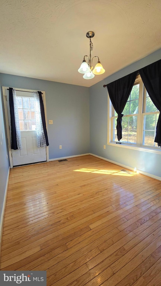 unfurnished room featuring light wood-type flooring, a textured ceiling, and a chandelier