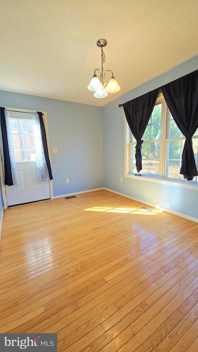 empty room featuring plenty of natural light, an inviting chandelier, and light hardwood / wood-style flooring