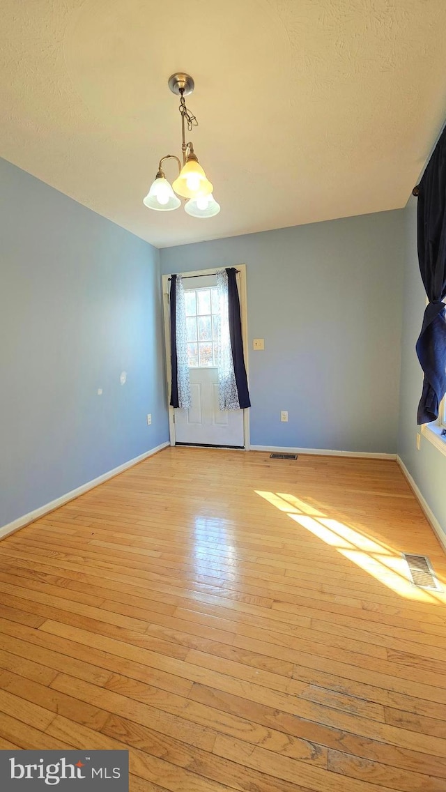 empty room featuring light wood-type flooring and an inviting chandelier