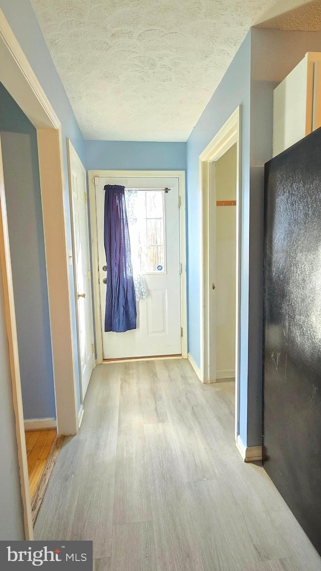 hall featuring light wood-type flooring and a textured ceiling