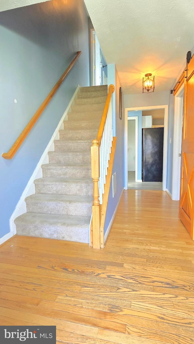 stairs featuring hardwood / wood-style floors, a barn door, and a textured ceiling