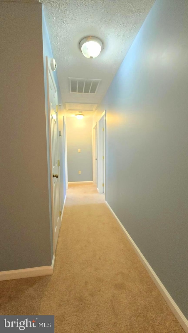 hallway featuring light colored carpet and a textured ceiling