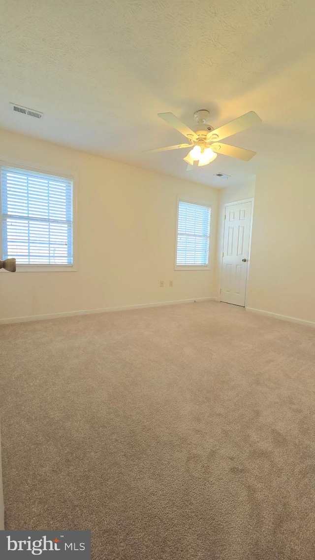 carpeted empty room with ceiling fan, a healthy amount of sunlight, and a textured ceiling