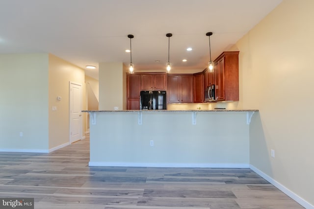 kitchen featuring black fridge, kitchen peninsula, hanging light fixtures, and light wood-type flooring