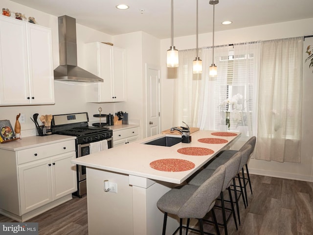 kitchen featuring wall chimney exhaust hood, a kitchen island with sink, white cabinets, dark hardwood / wood-style floors, and stainless steel range with gas cooktop