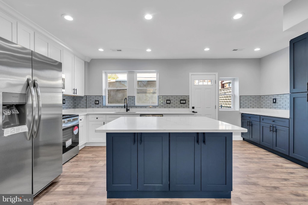 kitchen featuring sink, light hardwood / wood-style flooring, a kitchen island, white cabinetry, and stainless steel appliances