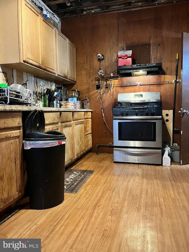 kitchen featuring light hardwood / wood-style floors, stainless steel range with gas cooktop, and wooden walls