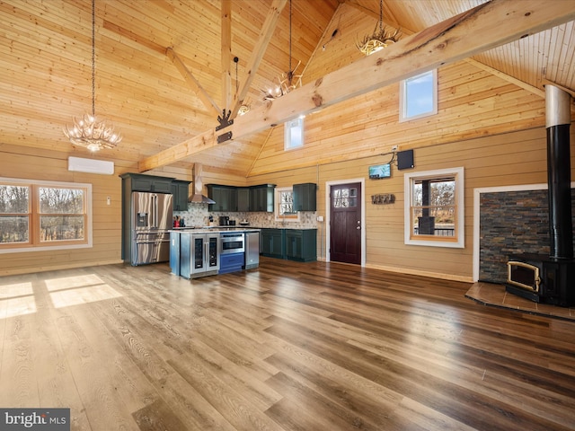 kitchen featuring a wood stove, hanging light fixtures, high vaulted ceiling, stainless steel refrigerator with ice dispenser, and wooden walls