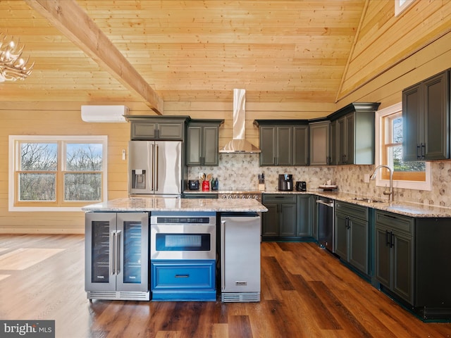 kitchen featuring sink, wall chimney exhaust hood, a healthy amount of sunlight, stainless steel appliances, and wood walls