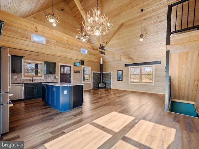 kitchen featuring pendant lighting, a wood stove, high vaulted ceiling, wooden walls, and stainless steel dishwasher