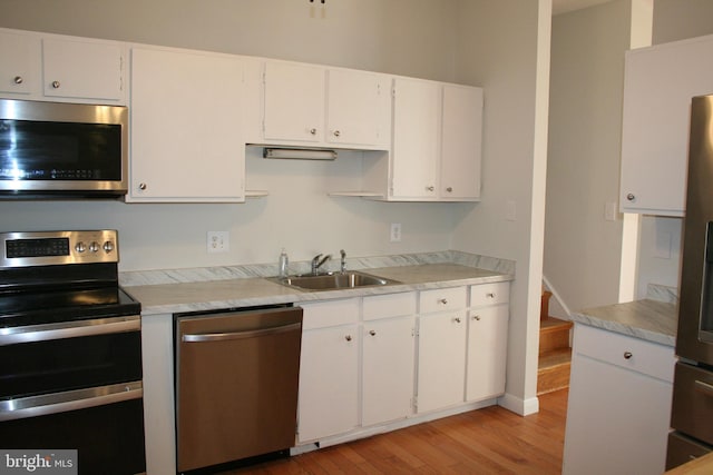 kitchen with stainless steel appliances, sink, white cabinets, and light hardwood / wood-style floors