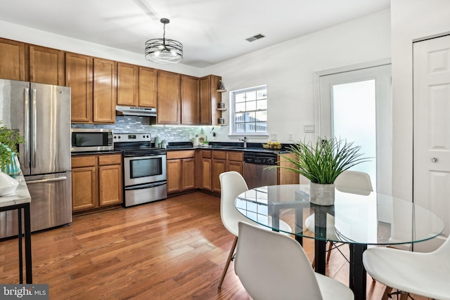 kitchen with dark hardwood / wood-style floors, decorative backsplash, appliances with stainless steel finishes, decorative light fixtures, and a chandelier