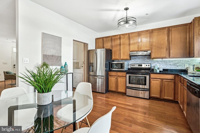 kitchen featuring backsplash, dark wood-type flooring, hanging light fixtures, washer / dryer, and stainless steel appliances