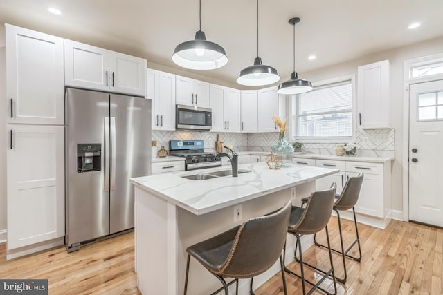 kitchen featuring a kitchen island with sink, white cabinets, light hardwood / wood-style flooring, light stone counters, and stainless steel appliances