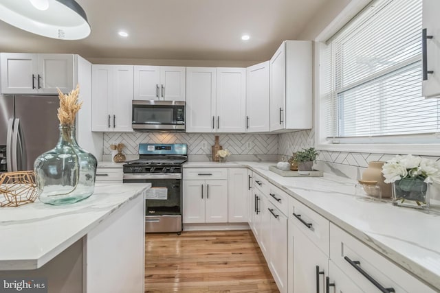 kitchen with backsplash, light hardwood / wood-style floors, white cabinetry, and stainless steel appliances