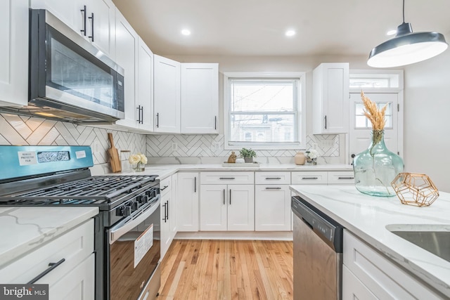 kitchen featuring decorative backsplash, appliances with stainless steel finishes, light stone counters, light hardwood / wood-style flooring, and white cabinetry