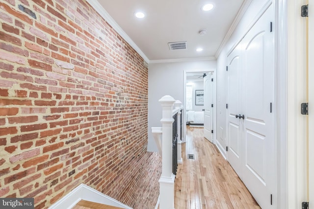 hallway featuring ornamental molding, brick wall, and light wood-type flooring