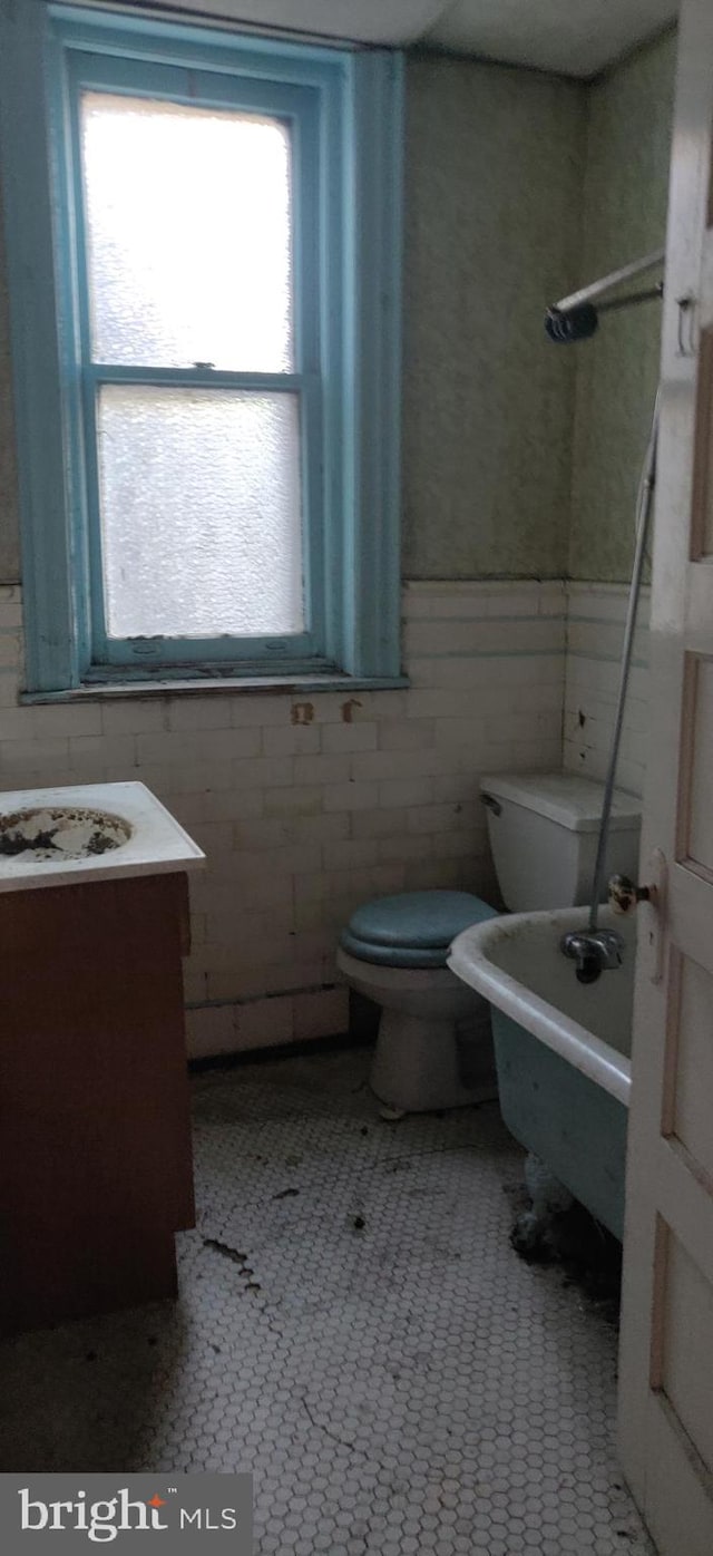 bathroom with vanity, a bath, tile patterned floors, toilet, and tile walls