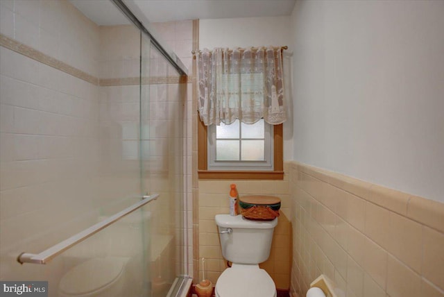 bathroom featuring toilet, a shower with door, and tile walls