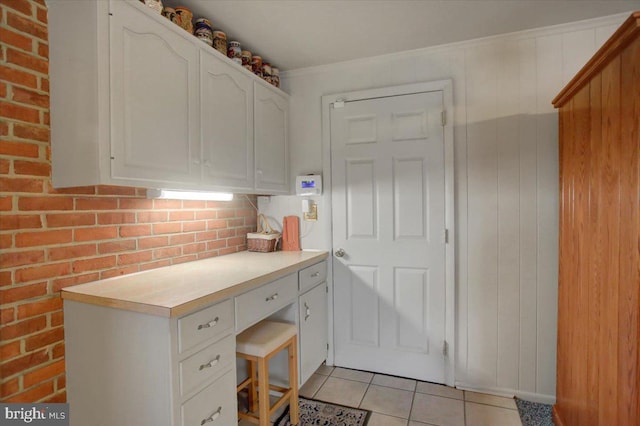 kitchen with white cabinets, light tile patterned floors, and brick wall