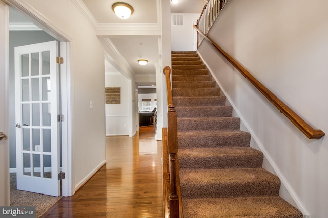 stairs with wood-type flooring and ornamental molding