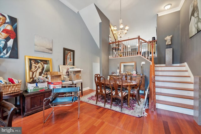 dining area with crown molding, a towering ceiling, wood-type flooring, and an inviting chandelier