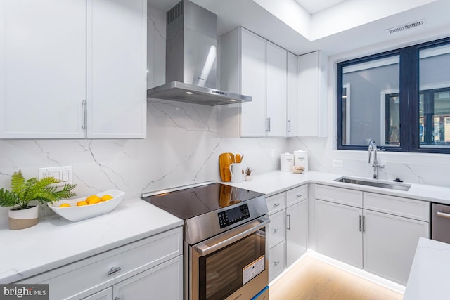 kitchen with stainless steel range, sink, white cabinets, and wall chimney range hood