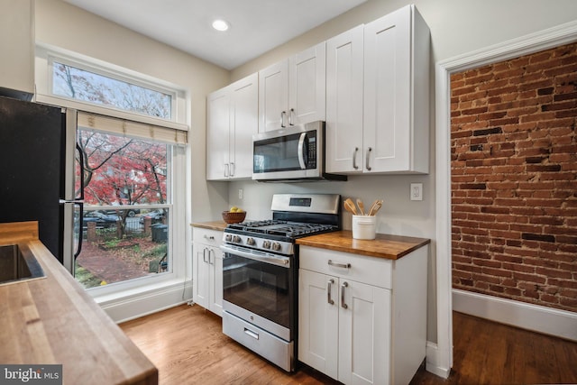 kitchen featuring appliances with stainless steel finishes, butcher block countertops, white cabinetry, and light hardwood / wood-style floors