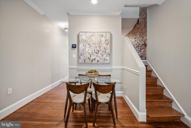 dining area with hardwood / wood-style flooring, ornamental molding, and brick wall