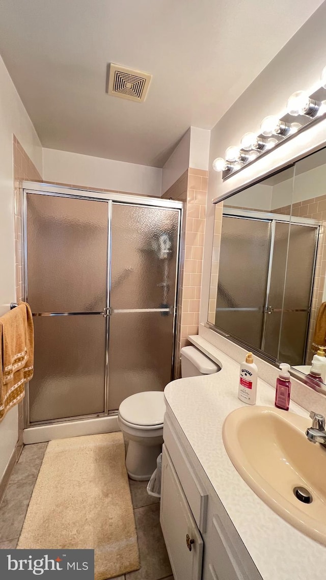 bathroom featuring tile patterned flooring, vanity, toilet, and a shower with shower door