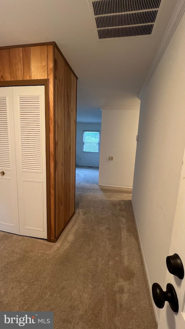 hallway with ornamental molding and dark colored carpet