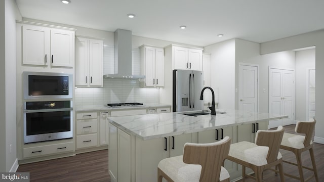 kitchen with white cabinetry, wall chimney range hood, stainless steel appliances, and a kitchen island with sink