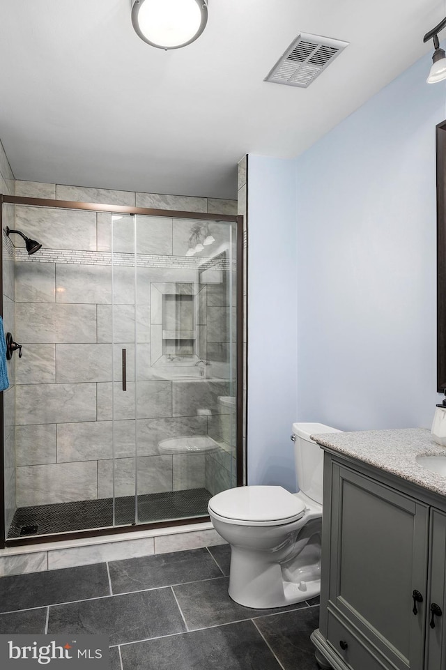 bathroom featuring tile patterned floors, vanity, a shower with shower door, and toilet