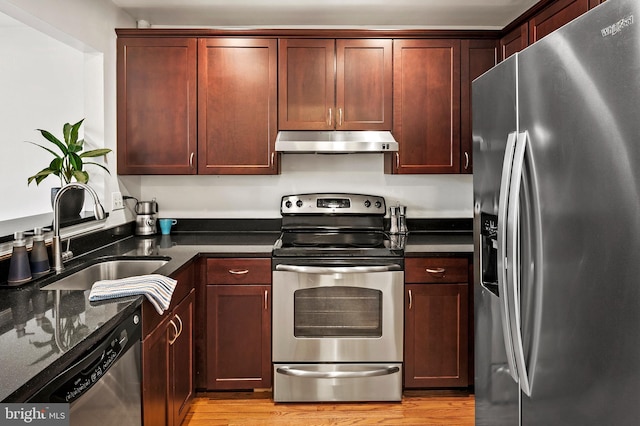 kitchen featuring appliances with stainless steel finishes, light hardwood / wood-style floors, dark stone countertops, and sink