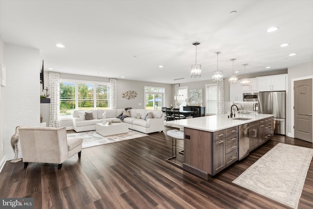 kitchen with white cabinetry, sink, hanging light fixtures, stainless steel appliances, and an island with sink